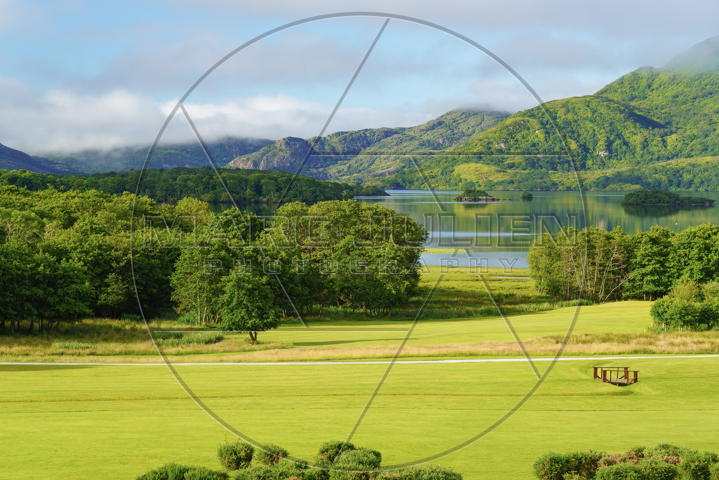 Grüner Golfplatz am See, umgeben von nebelverhangenen Bergen